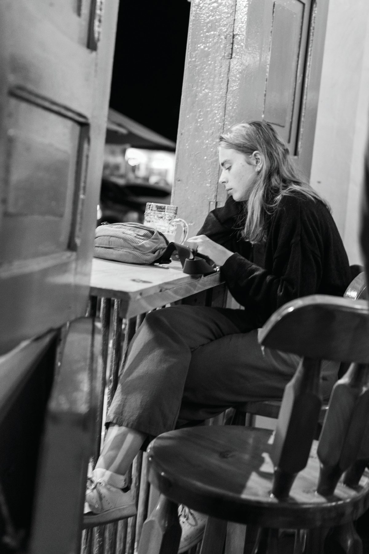 A woman sitting at an open-air counter looking at her phone while the street lies beyond her.