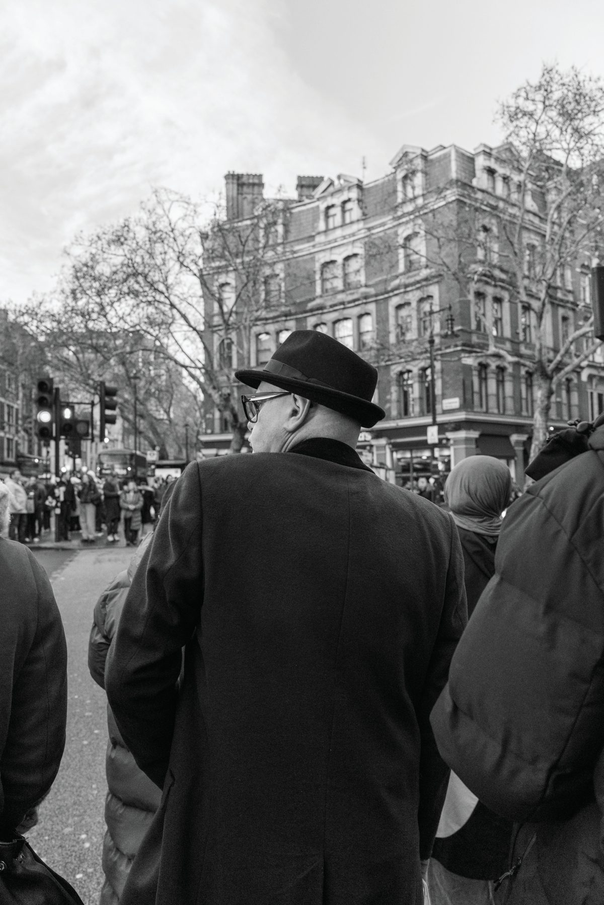 A man in a dark brimmed hat walking through a crowded London street seen from behind.