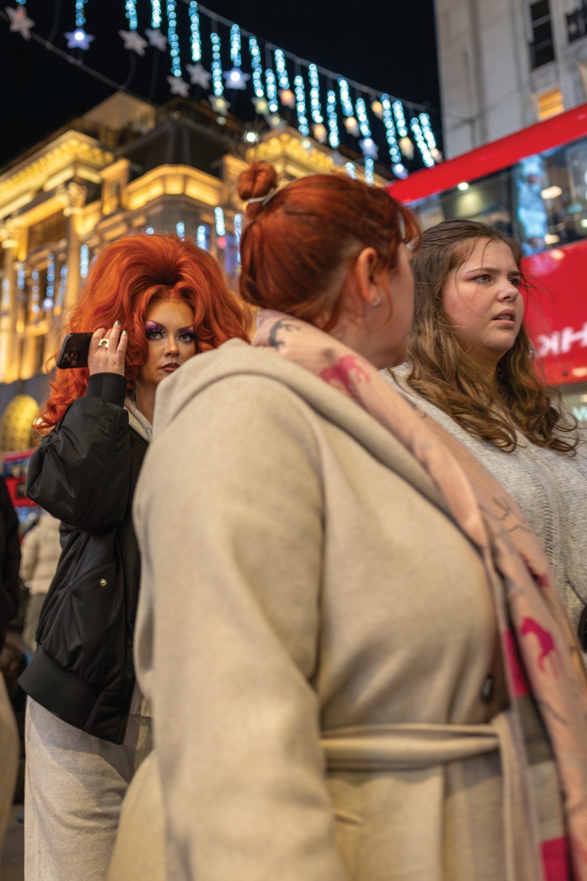 A red-haired woman looking across a crowded, brightly lit Oxford Street at night.