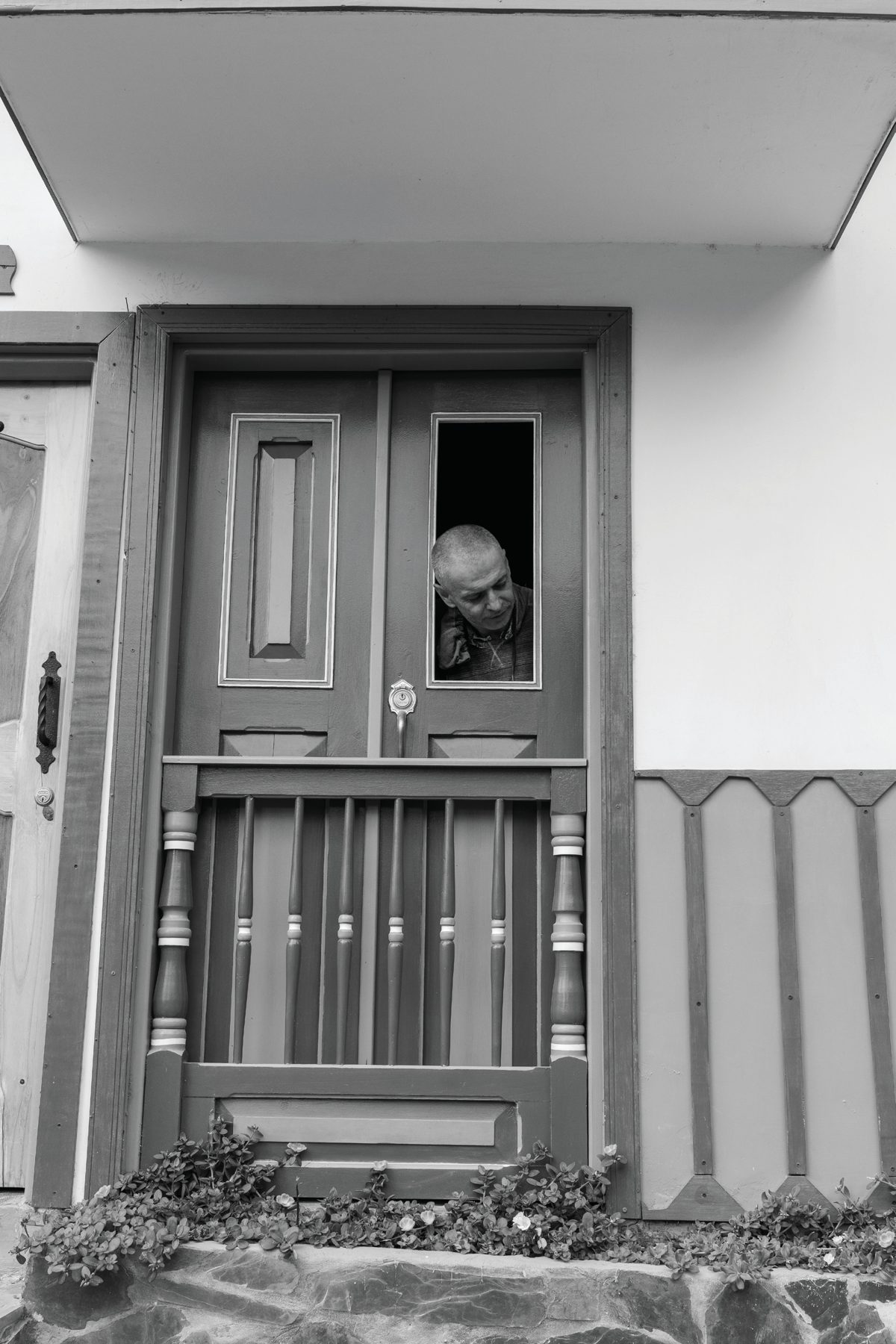 A child peering through an open upper section of a simple door in a white house.