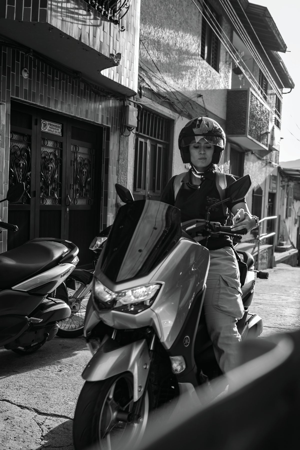 A helmeted rider paused on a scooter along a sunlit street in San Rafael, Colombia.