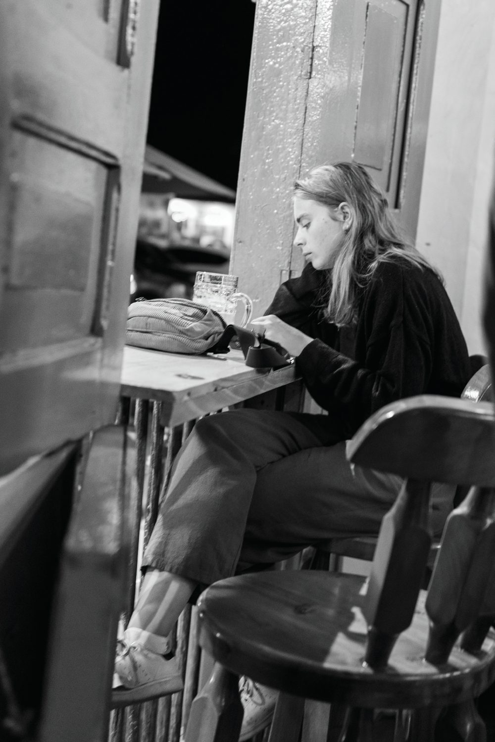 A woman sitting at an open-air counter looking at her phone while the street lies beyond her.