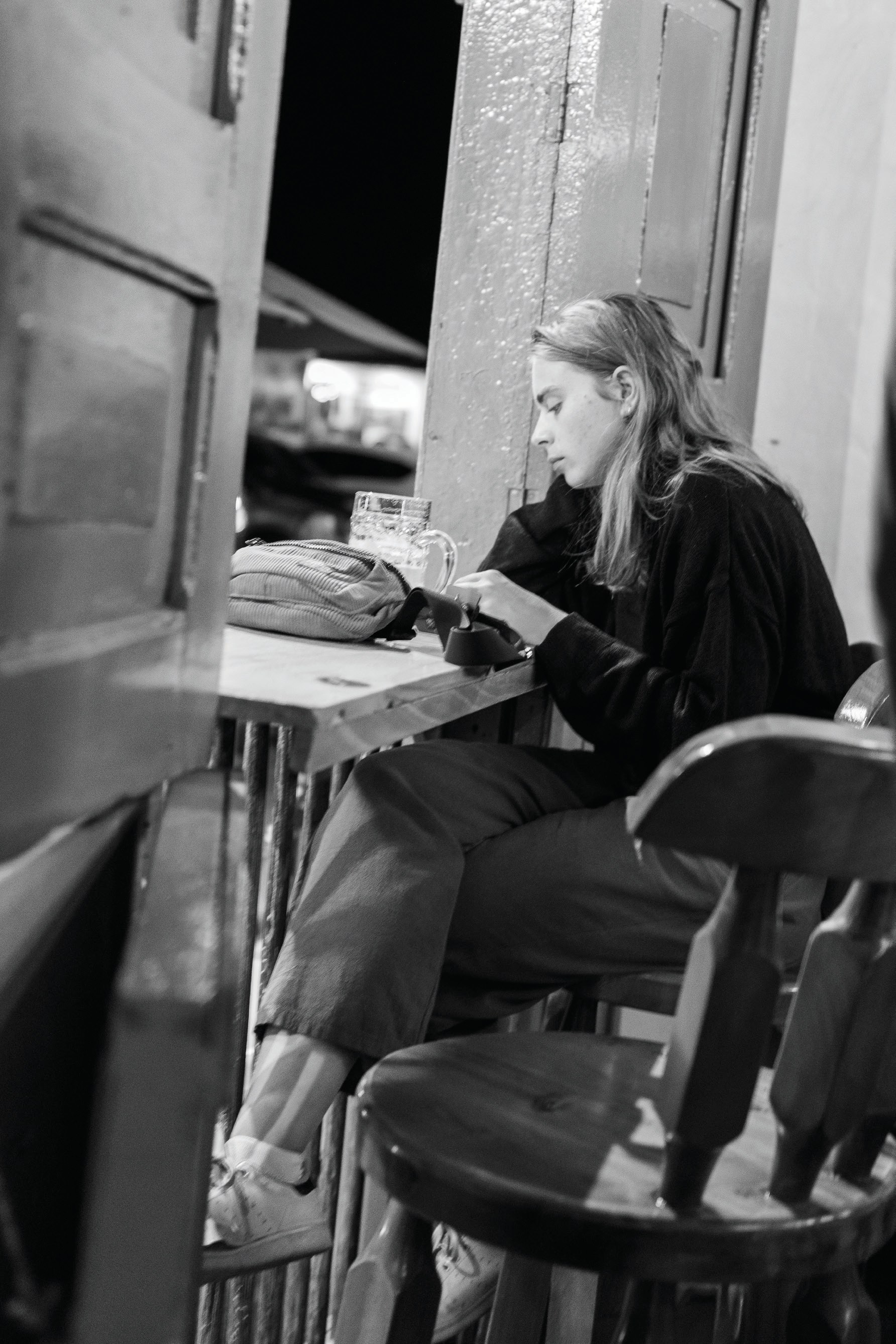 A woman sitting at an open-air counter looking at her phone while the street lies beyond her.