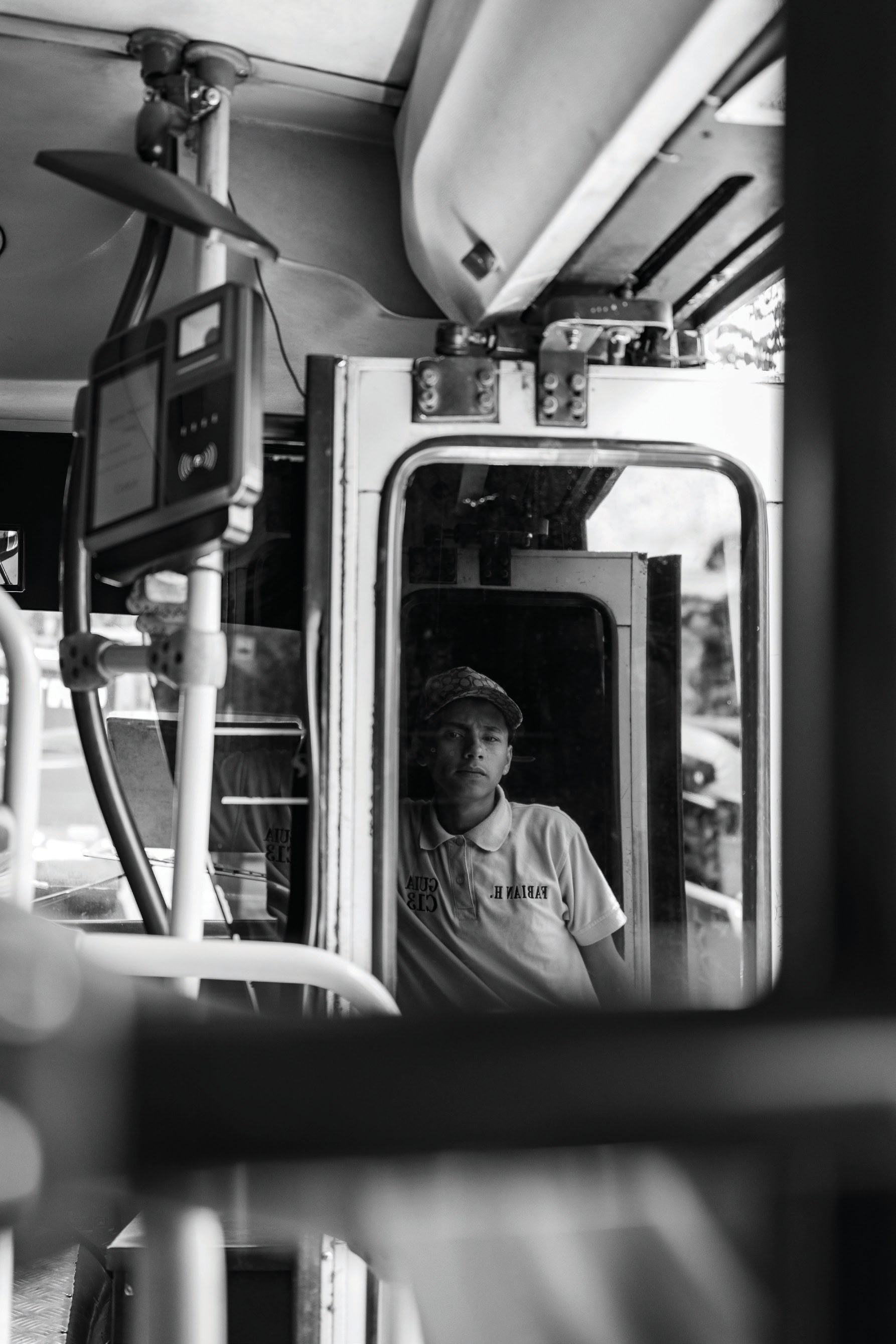 A young guide seated near the front of a bus, reflected in its mirror and framed by the vehicle interior.