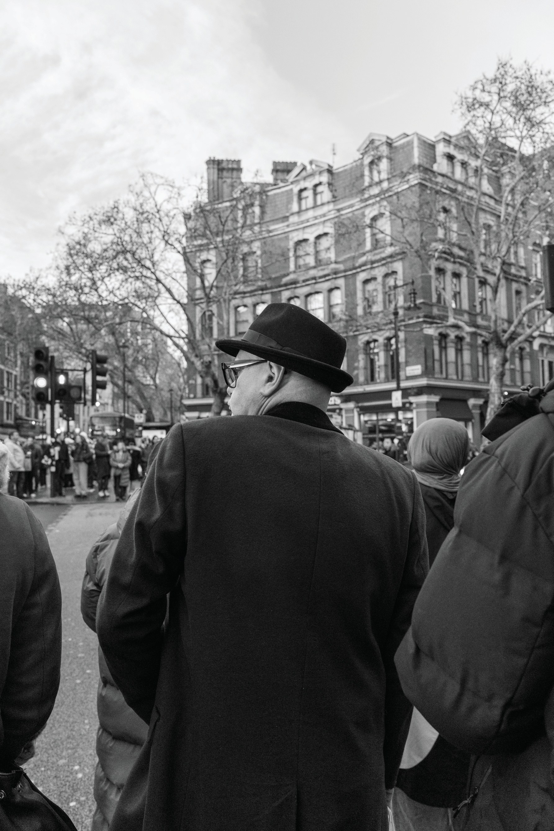 A man in a dark brimmed hat walking through a crowded London street seen from behind.