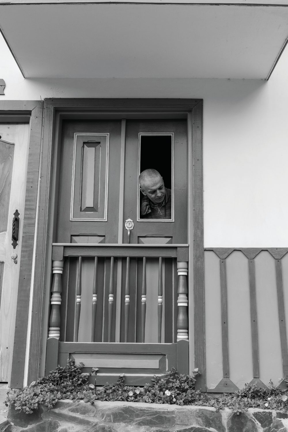 A child peering through an open upper section of a simple door in a white house.