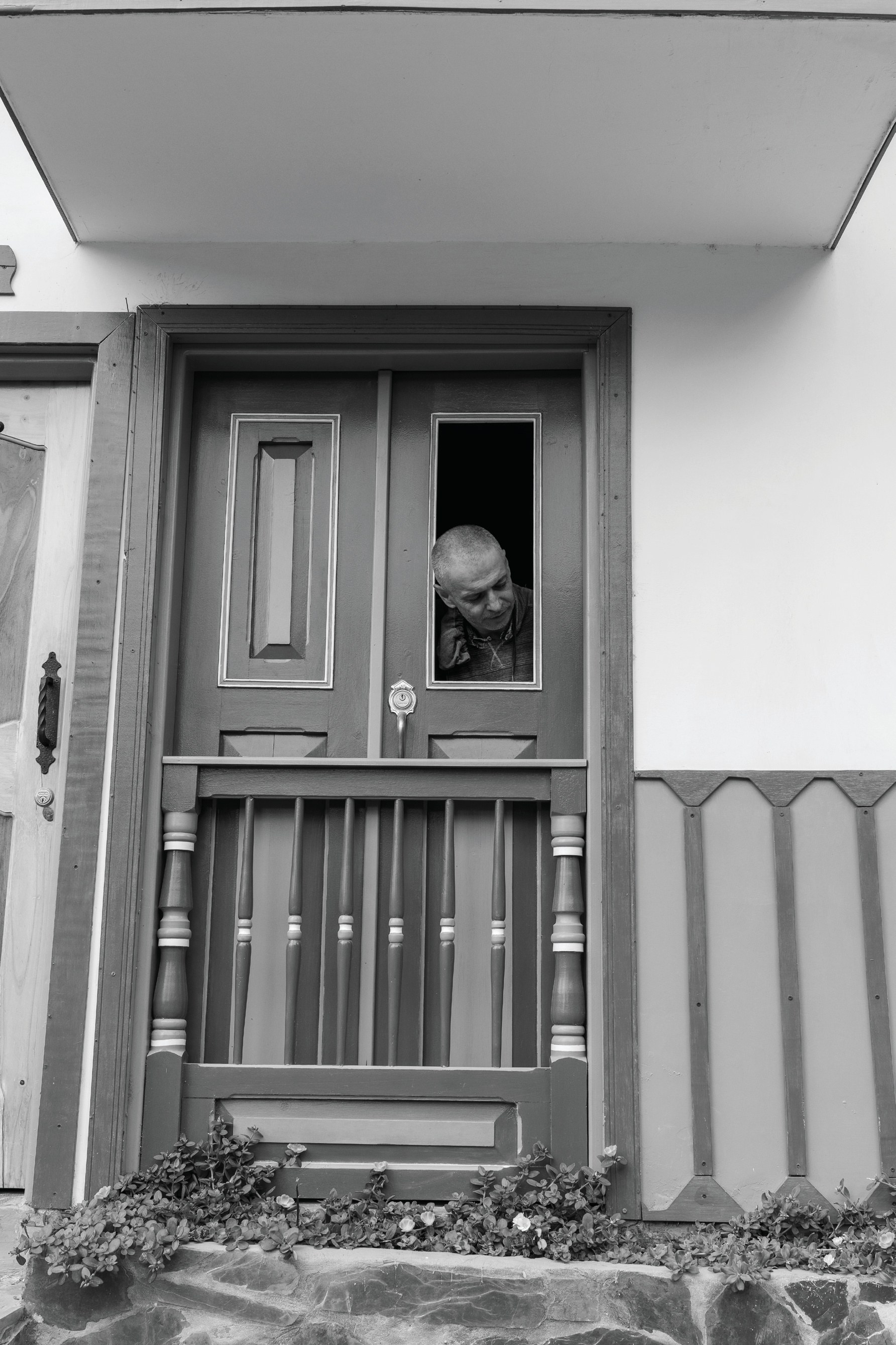 A child peering through an open upper section of a simple door in a white house.