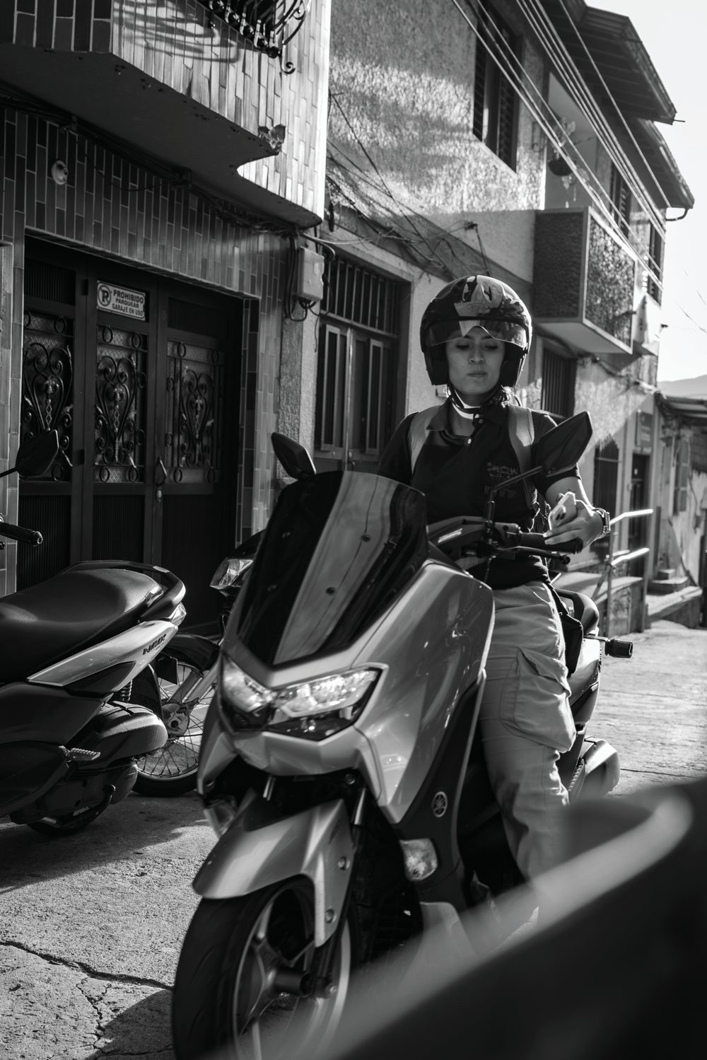 A helmeted rider paused on a scooter along a sunlit street in San Rafael, Colombia.