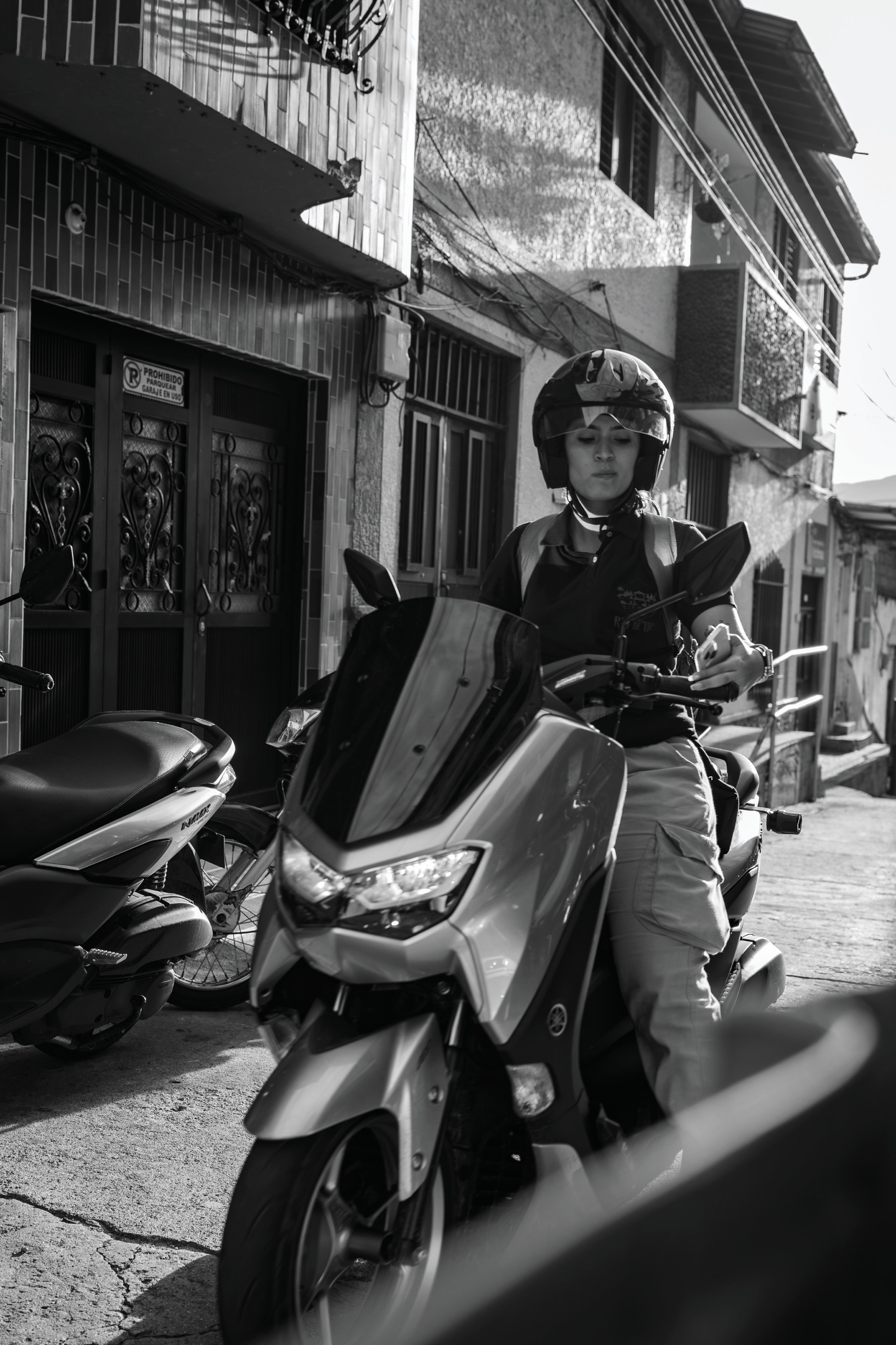 A helmeted rider paused on a scooter along a sunlit street in San Rafael, Colombia.